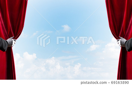 Cloudy landscape behind red curtain and hand holding it Cloudy landscape behind red curtain and hand holding it 69163890