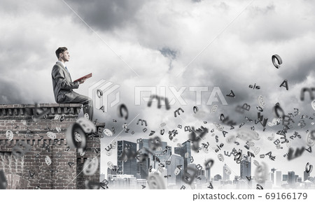 Man on roof edge reading book and symbols flying around 69166179