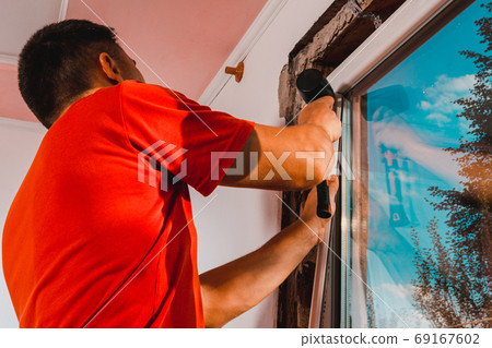 Window installation, a new plastic window in a private house, the master uses a rubber hammer to install the window. 69167602