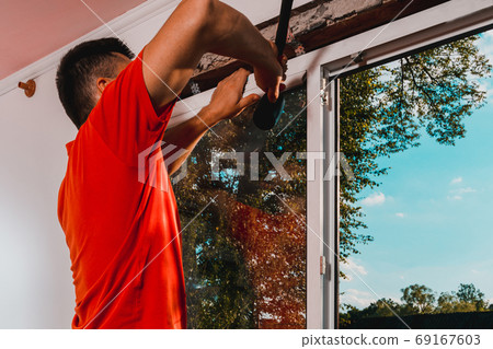 Window installation, a new plastic window in a private house, the master uses a rubber hammer to install the window. Window installation, a new plastic window in a private house, the master uses a rubber hammer to install the window. 69167603