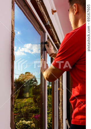 The worker inserts glass into the window frame, triple glazing of the plastic window, insulation and insulation. 69167605