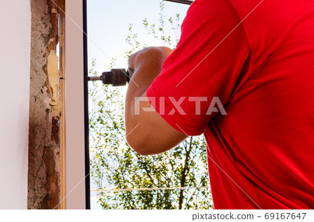 A man in his own house installs a plastic window, installs a new window, a worker uses an electric drill. 69167647