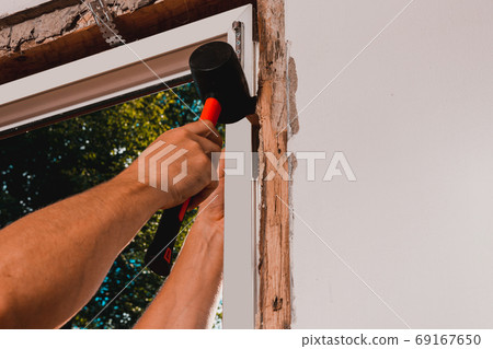 Window installation, a new plastic window in a private house, the master uses a rubber hammer to install the window. 69167650