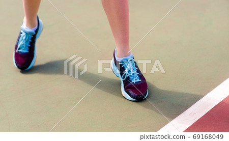 Legs of young girl in a closed tennis court with racket, sport shoes Legs of young girl in a closed tennis court with racket, sport shoes 69168049