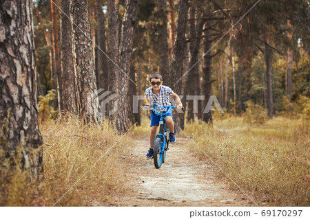 Happy kid cyclist rides in the forest on a bike. Happy kid cyclist rides in the forest on a bike. 69170297
