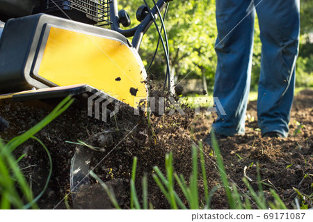 The man tills the soil with the motor cultivator The man tills the soil with the motor cultivator 69171087