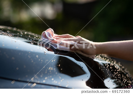 hand wiping water on black car 69172360