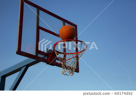An orange basketball is flying into the basket on an open area against the sky. 69174892