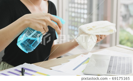 Young woman cleaning the surface of laptop with alcohol spray and fabric at home 69175165