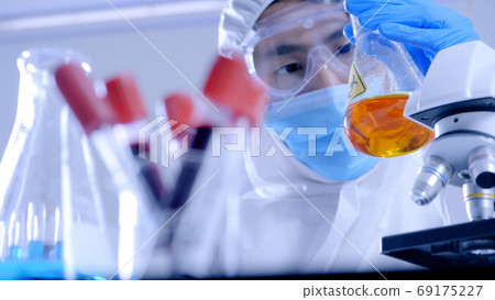 Scientist in PPE suite doing some research checking a liquid in a test tube at laboratory. 69175227