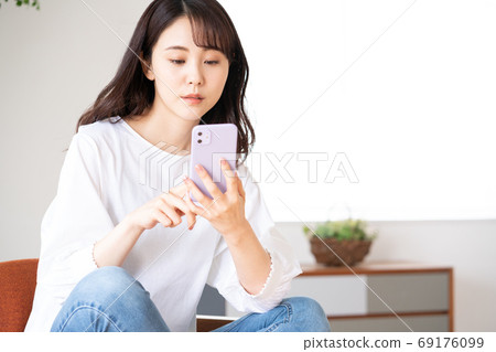 焦慮的臉年輕女子坐在客廳裡拿著智能手機的椅子上 69176099