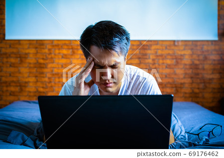 headache, tense young asian man working on laptop computer in bedroom at night headache, tense young asian man working on laptop computer in bedroom at night 69176462