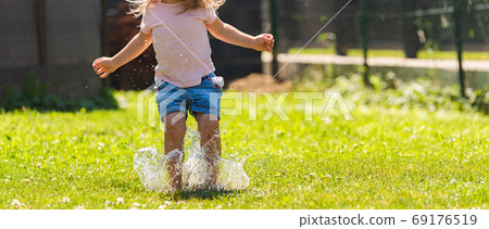 Happy child running through wet lawn splashinh 69176519