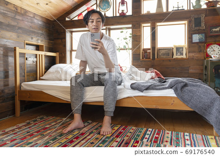 年輕人坐在床上，看著智能手機 69176540