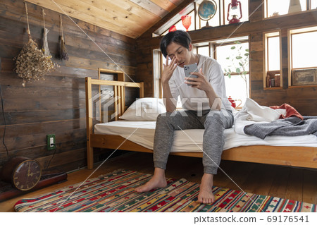 年輕人坐在床上，看著智能手機 69176541