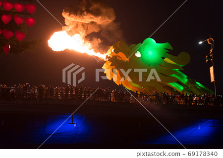 The head of the bridge dragon spews smoking fire in the darkness of night in front of the spectators crowded the bridge. 69178340