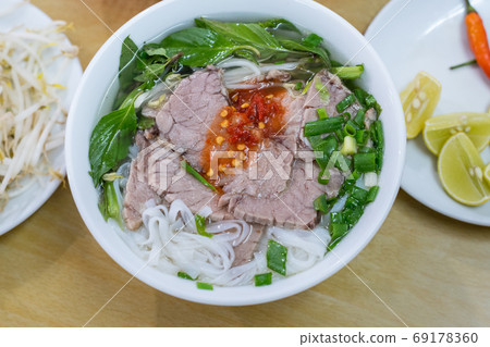 Soup pho in a budget restaurant in Danang city, Vietnam for 35 000 dongs. Noodles, sliced boiled beef, basil leaves, chopped spring onion. Sprouts, chili and pieces of lime on the plate. 69178360