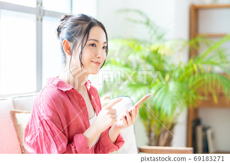 A woman who operates a smartphone while relaxing on the sofa. A woman who operates a smartphone while relaxing on the sofa. 69183271