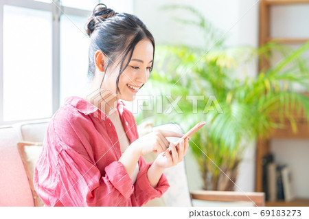 一個女人在沙發上放鬆的同時操作智能手機。 一個女人在沙發上放鬆的同時操作智能手機。 69183273