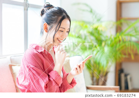 A woman who operates a smartphone while relaxing on the sofa. 69183274