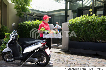 Asian delivery man wearing face mask and gloves delivering parcel box to recipient during COVID-19  69183947