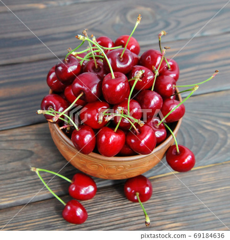 Sweet cherry berries in a clay pot on a wooden table. View from above 69184636