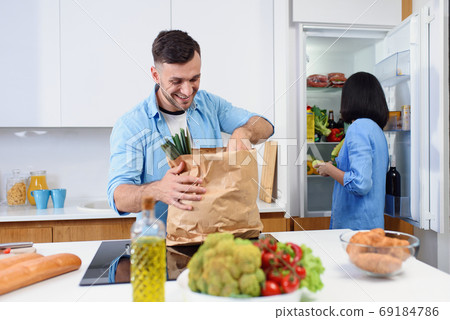 Attractive couple of two young people unpacking together fresh products from market in kitchen. Happy family concept. Attractive couple of two young people unpacking together fresh products from market in kitchen. Happy family concept. 69184786