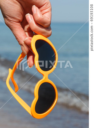 Hand of woman with sunglasses in shape of heart on beach. Summer time 69193108