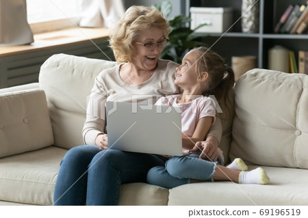 Excited mature grandmother and granddaughter using laptop, having fun 69196519
