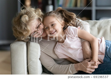 Laughing mature grandmother playing with pretty little granddaughter on couch Laughing mature grandmother playing with pretty little granddaughter on couch 69196537