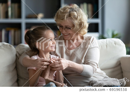 Smiling loving mature grandmother teaching little granddaughter knitting Smiling loving mature grandmother teaching little granddaughter knitting 69196538