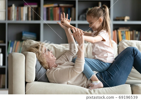 Happy mature grandmother playing with little granddaughter on couch Happy mature grandmother playing with little granddaughter on couch 69196539