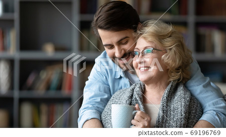 Smiling young man hugging mature mother drinking tea 69196769