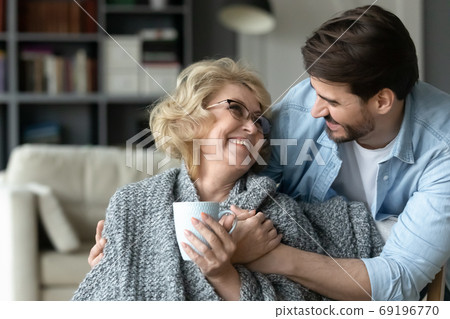 Smiling mature woman holding cup, hugging with adult son 69196770