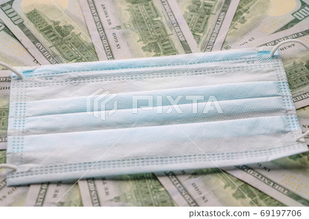Medical mask on dollar bills. Fight against COVID - 19. The fall of economies due to the virus. Medical mask on dollar bills. Fight against COVID - 19. The fall of economies due to the virus. 69197706