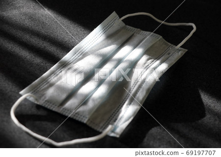 Medical mask on a dark background. Light rays hit the mask. Global fight against COVID-19 virus Medical mask on a dark background. Light rays hit the mask. Global fight against COVID-19 virus 69197707