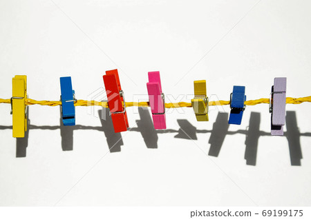 colored wooden clothespins on a yellow rope on a white background with shadow 69199175