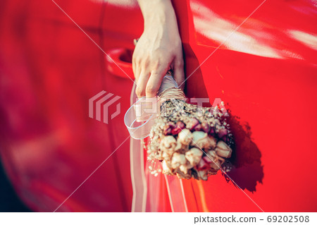 Bride holding the wedding bouquet and wave it from the window of the red car. 69202508