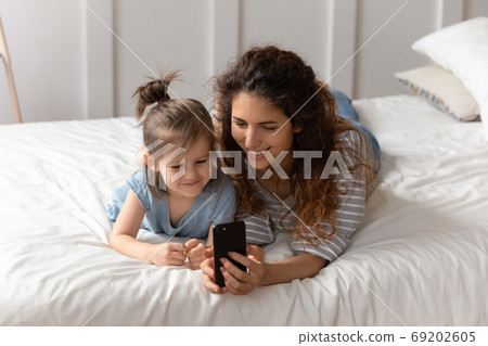 Mother lying on bed with daughter having fun using smartphone 69202605