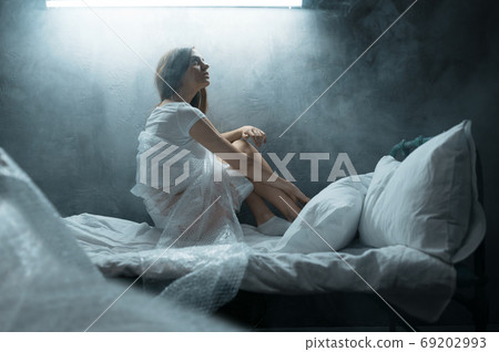 Psycho woman in packaging film sitting in bed 69202993