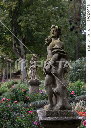 An old statue of a goddess stands in a botanical garden in Rothenburg ob der Tauber, covered with green moss, among the flowers. An old statue of a goddess stands in a botanical garden in Rothenburg ob der Tauber, covered with green moss, among the flowers. 69204696