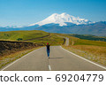 A woman walks along the road with her arms outstretched, panorama against the background of mount Elbrus, Caucasus Russia.  69204779