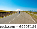 A woman walks along the road with her arms outstretched, panorama against mount Elbrus, Caucasus Russia 69205184