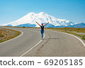 A woman walks along the road with her arms outstretched, panorama against mount Elbrus, Caucasus Russia 69205185