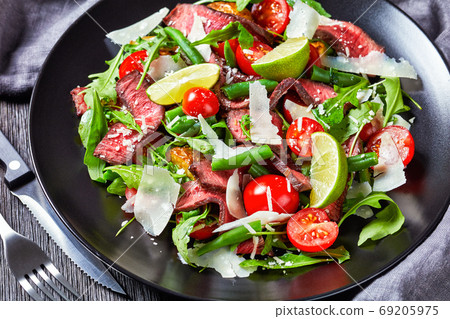 Beef tagliata salad on a black plate, close-up 69205975