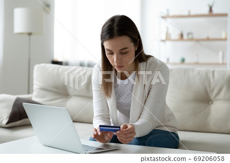 Focused young woman entering banking card information in computer application. 69206058