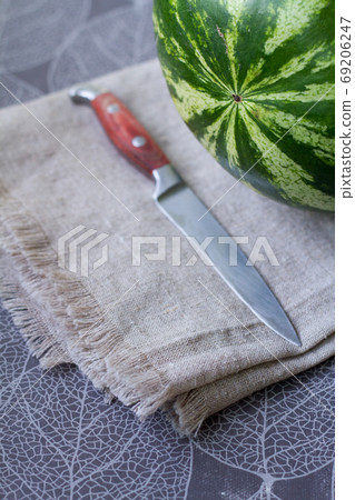 Fresh watermelon on linen tablecloth next to knife, preparing for picnic, selective focus Fresh watermelon on linen tablecloth next to knife, preparing for picnic, selective focus 69206247