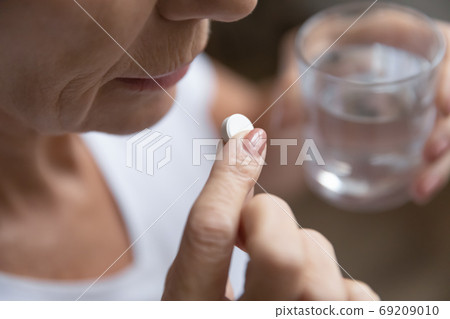 Close up senior woman taking pill, holding glass of water 69209010