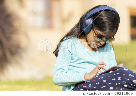 Little girl listening to music on the smartphone with her headph 69211969