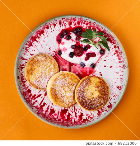 Cottage cheese pancakes or fritters served with sour cream and fruity sauce over orange background. Top view, copy space. Cottage cheese pancakes or fritters served with sour cream and fruity sauce over orange background. Top view, copy space. 69212006
